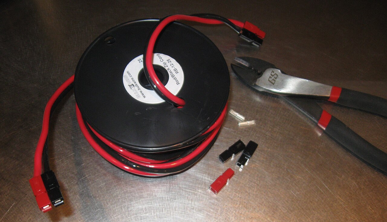 Anderson Powerpole housings and contacts on a workbench beside a wire spool and crimp tool