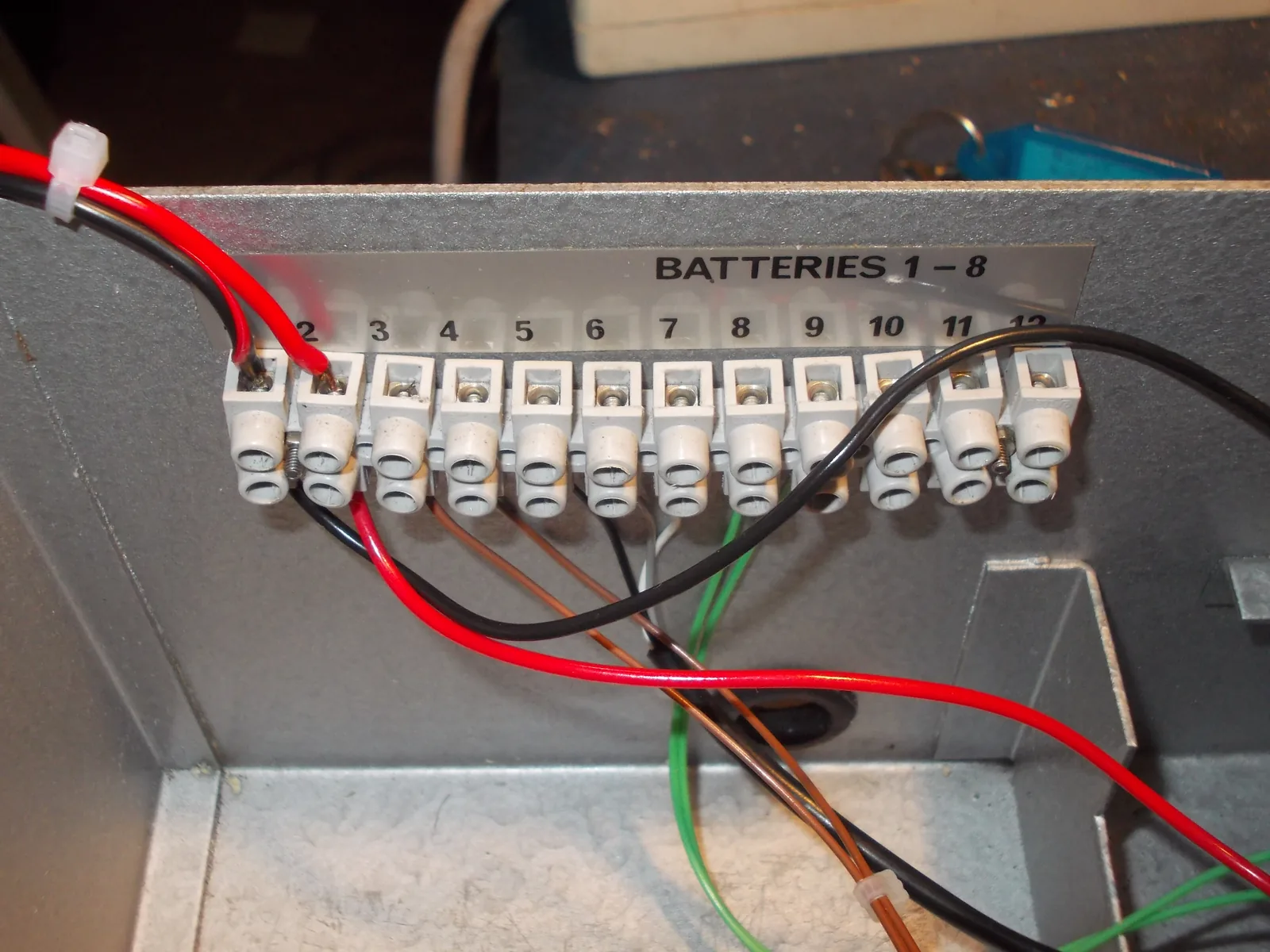 A labeled screw terminal strip mounted inside a metal cabinet with several power and signal wires landed on numbered positions