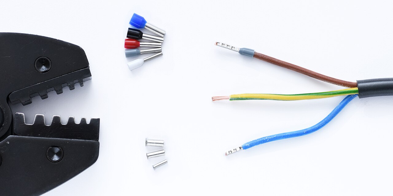 A ferrule crimper beside assorted wire ferrules and a cable with ferrule-terminated conductors