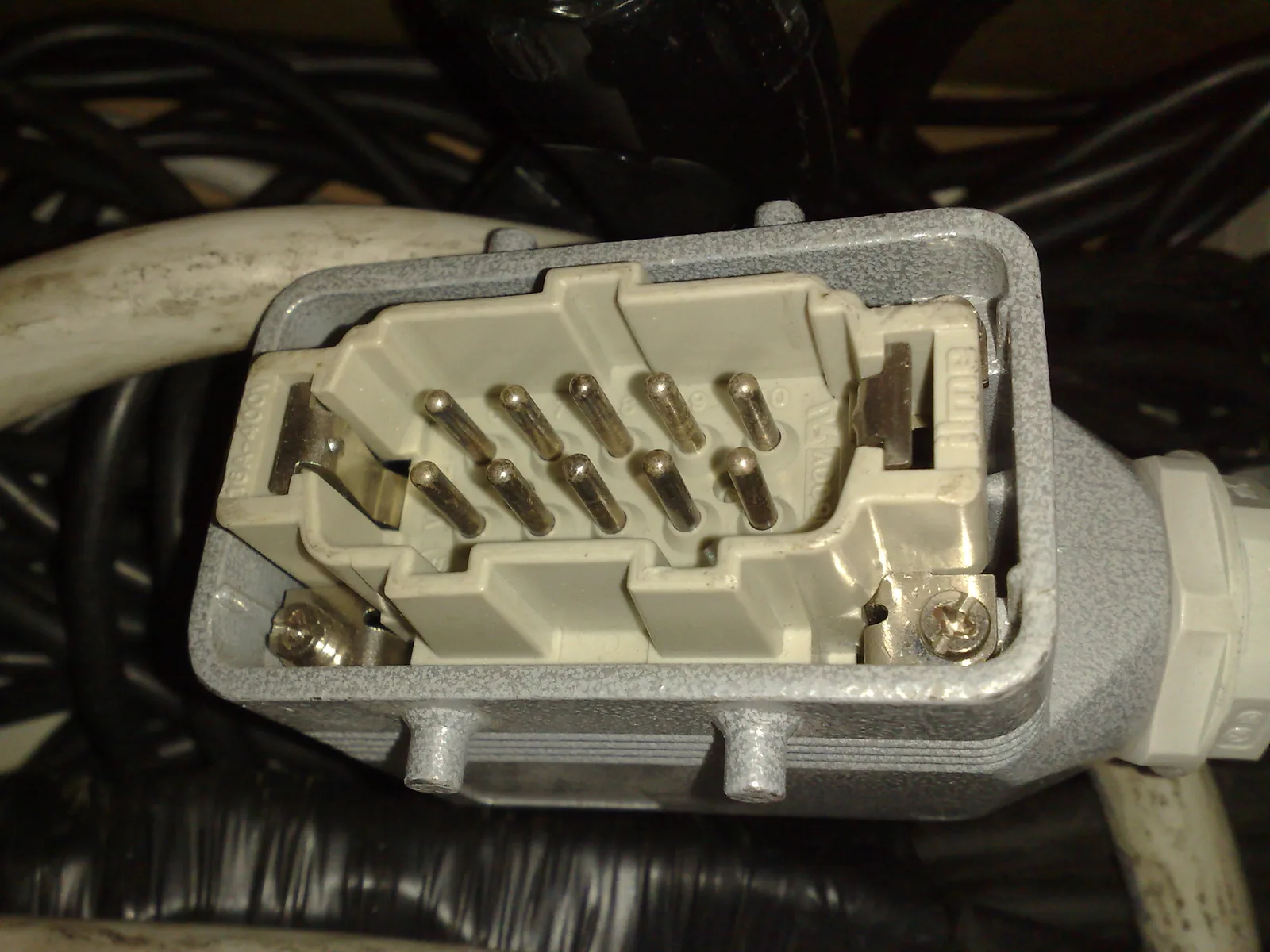 An open 10-pole heavy-duty rectangular cable connector showing the pin insert, protective metal shell, and cable entry