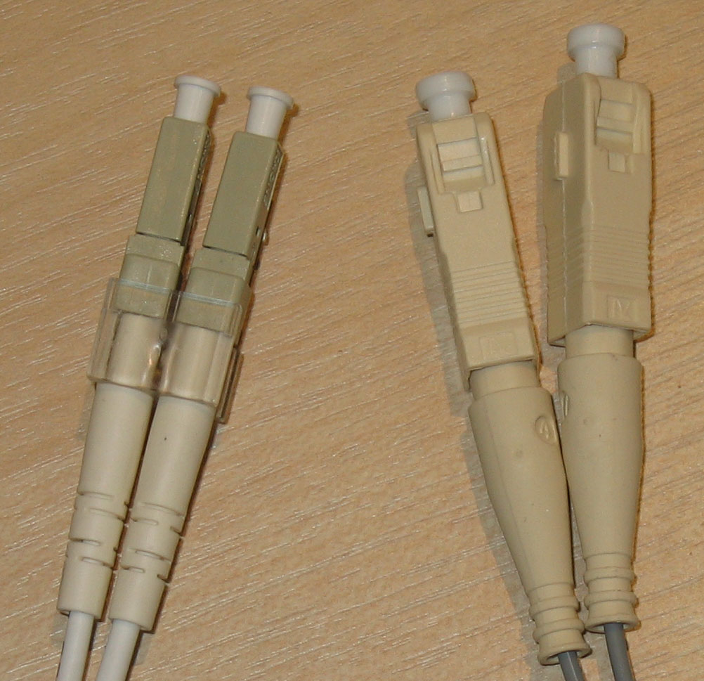 Two narrow LC fiber-optic connectors beside two larger square SC fiber-optic connectors, all with protective ferrule caps installed