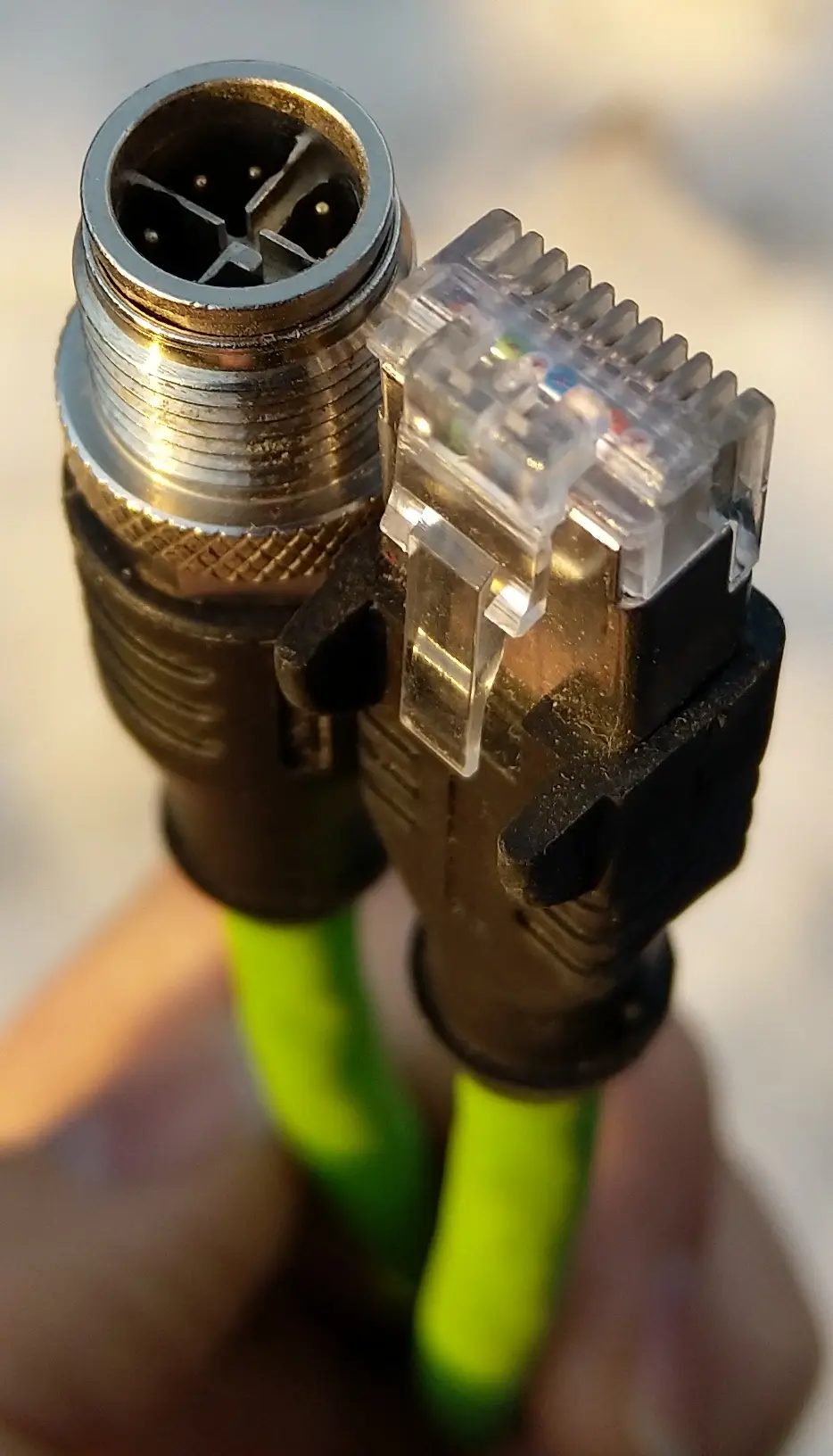 An M12 X-coded plug next to a clear RJ45 plug on green industrial Ethernet cable