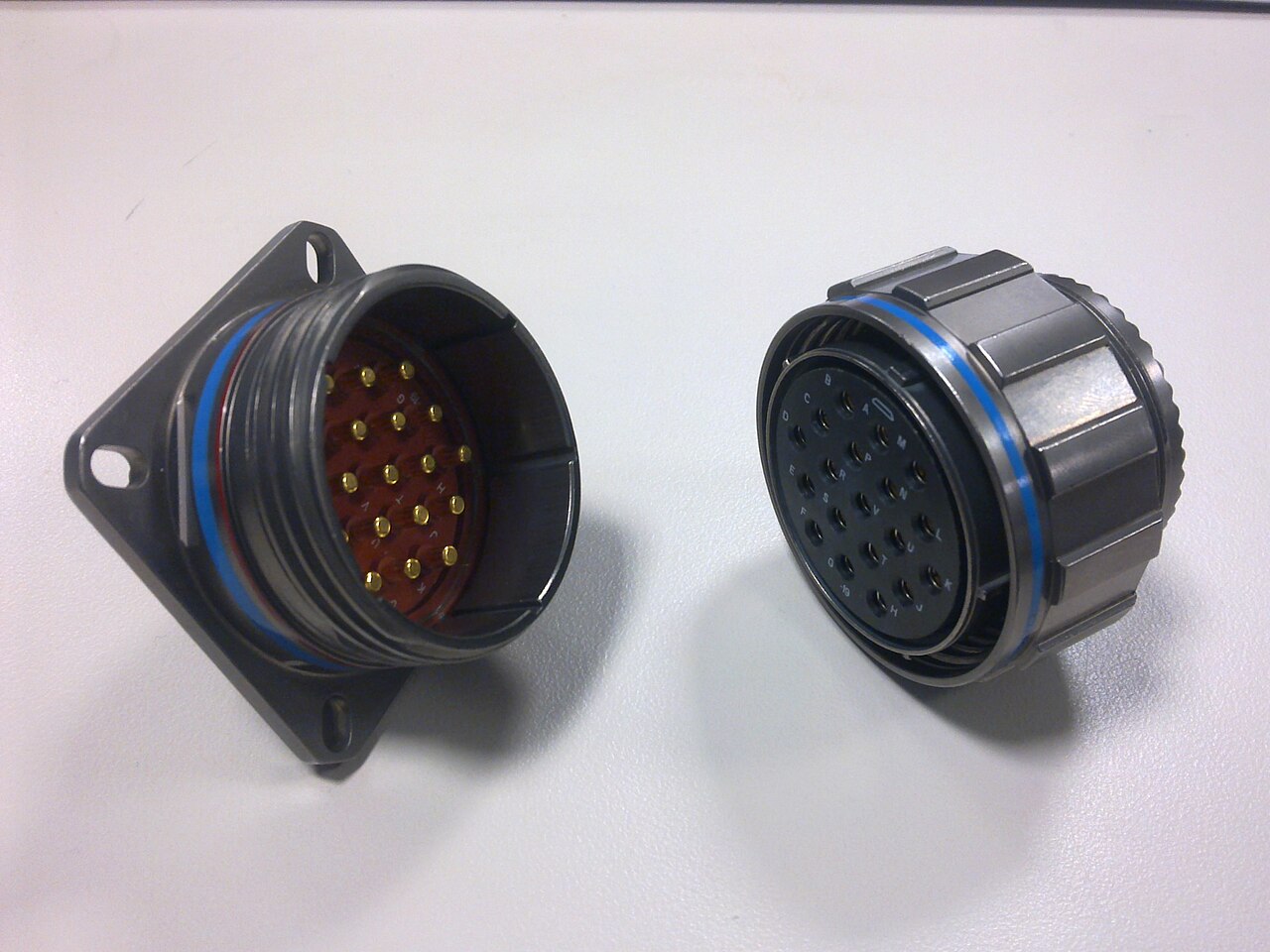 A 38999-style square-flange panel receptacle with gold pin contacts next to its mating plug with knurled coupling nut
