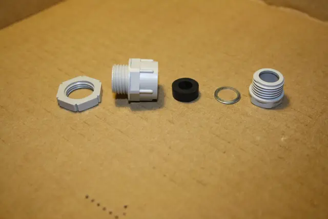 A disassembled cable gland showing its body, seal, washer, and compression nut
