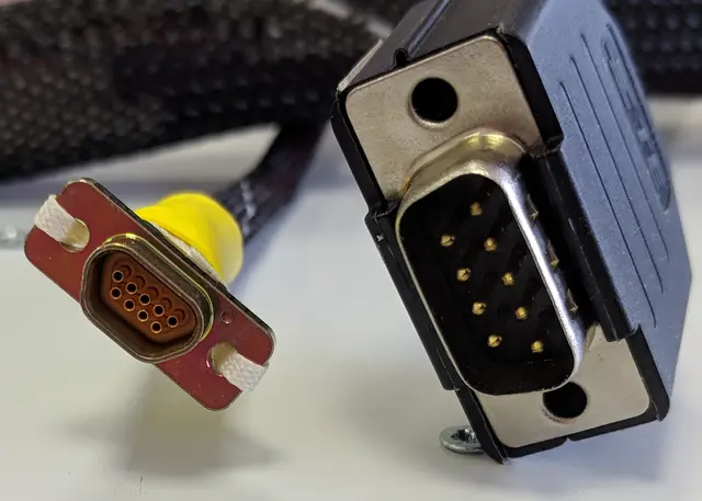 A compact Micro-D connector beside a larger DE-9 connector for scale